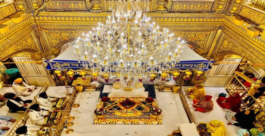 Sikh devotees offering prayers inside the beautifully adorned golden shrine with intricate designs and a grand chandelier at the Golden Temple.