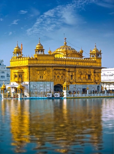 Golden Temple in Amritsar reflecting in the serene waters of the surrounding holy pool under a bright blue sky.