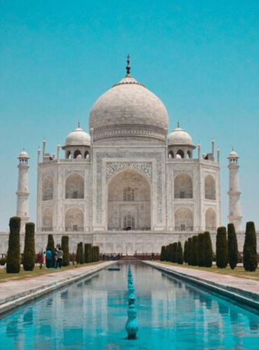 Majestic view of the Taj Mahal reflecting in the central pool under a clear blue sky.